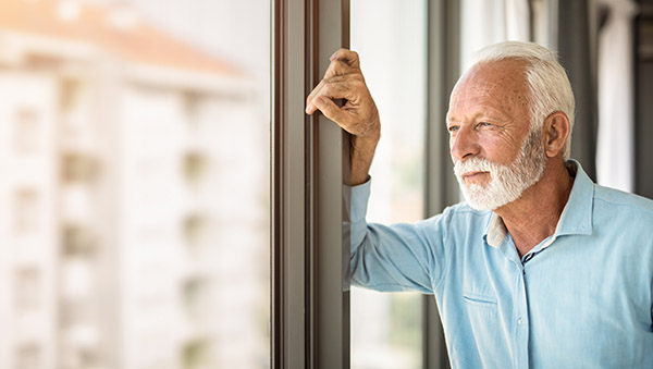 Serious senior man looking through window of his apartment.