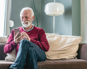 Senior men in a red sweater sitting in a living room at home and he is using smart phone