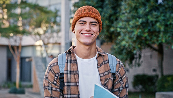 University, student and man in portrait outdoor on campus with book for education, learning and scholarship. Gen z, person and happy at college for studying, knowledge or backpack for research