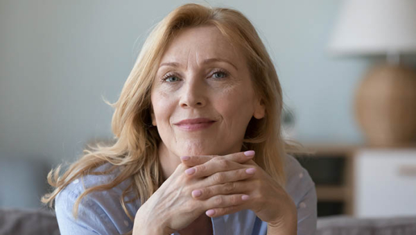 Close up portrait attractive middle-aged woman resting on cozy sofa alone at home staring at camera