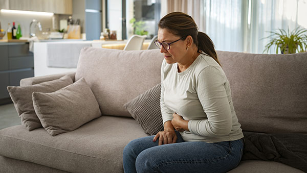 Woman holding stomach in pain while sitting on a couch.